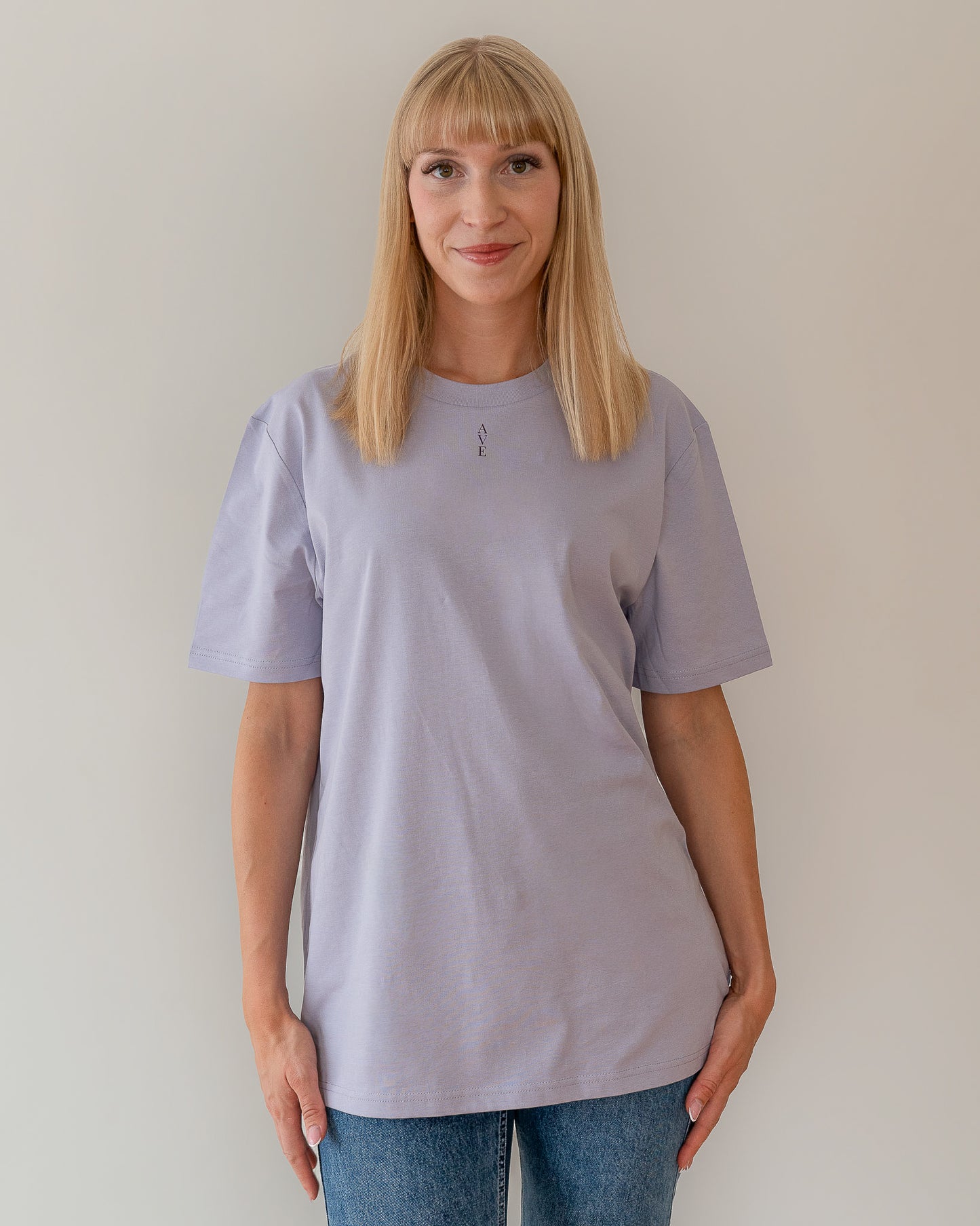 TESSERA t-shirt in lavender, worn by a woman, tucked loose, AVE lettering at the neckline