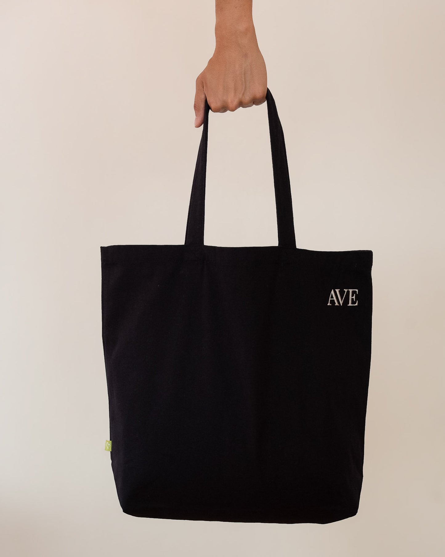 AVE tote bag in black, held by hand, AVE embroidery in the corner