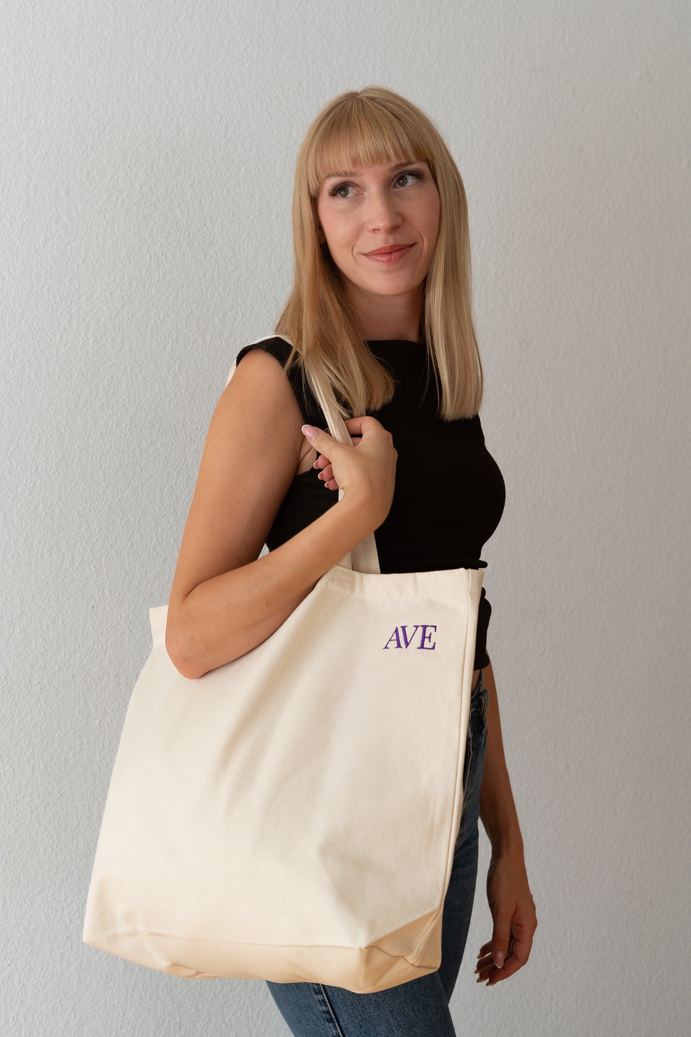 AVE tote bag in beige, worn over the shoulder by a woman