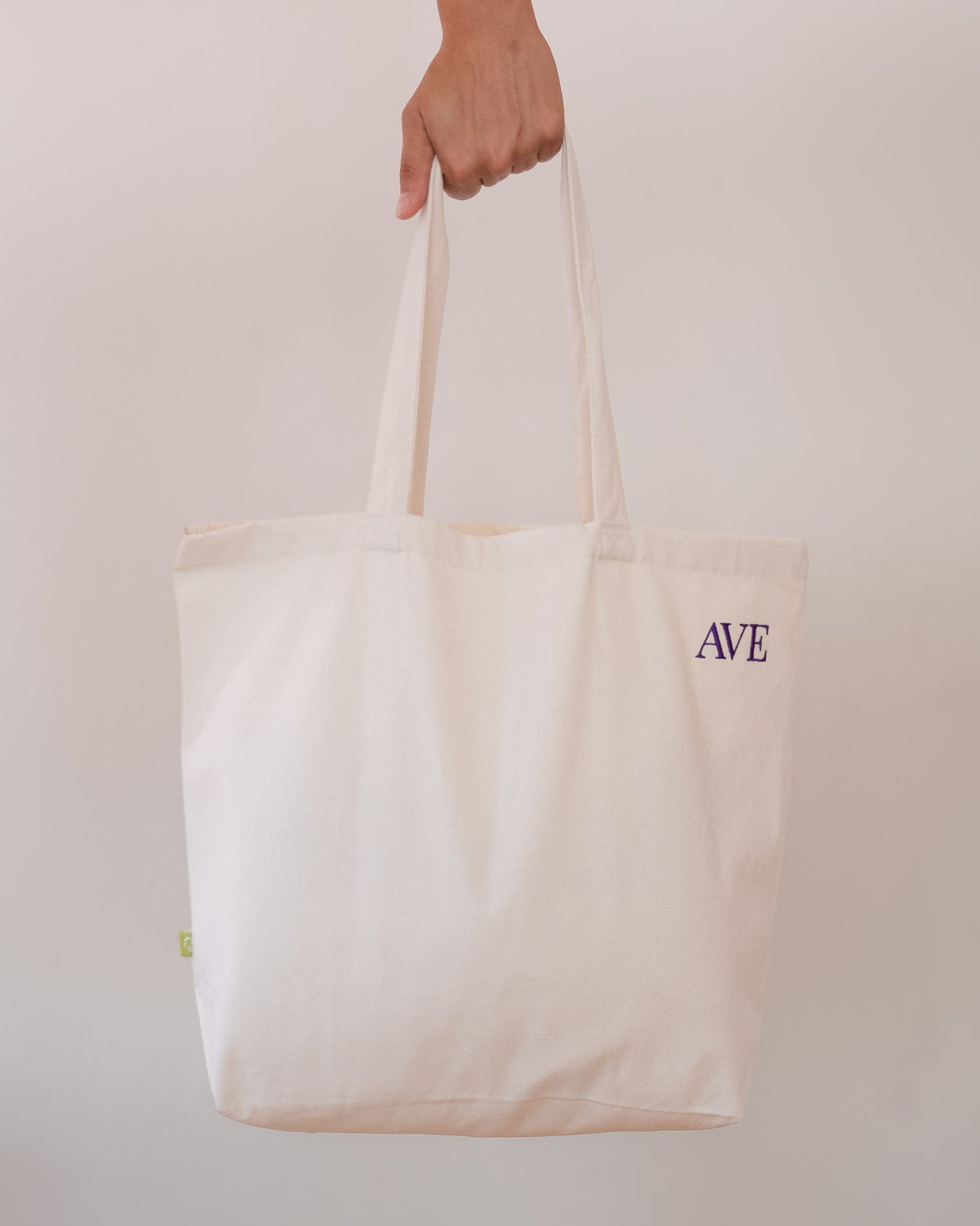 AVE tote bag in beige, held by hand, AVE embroidery in the corner