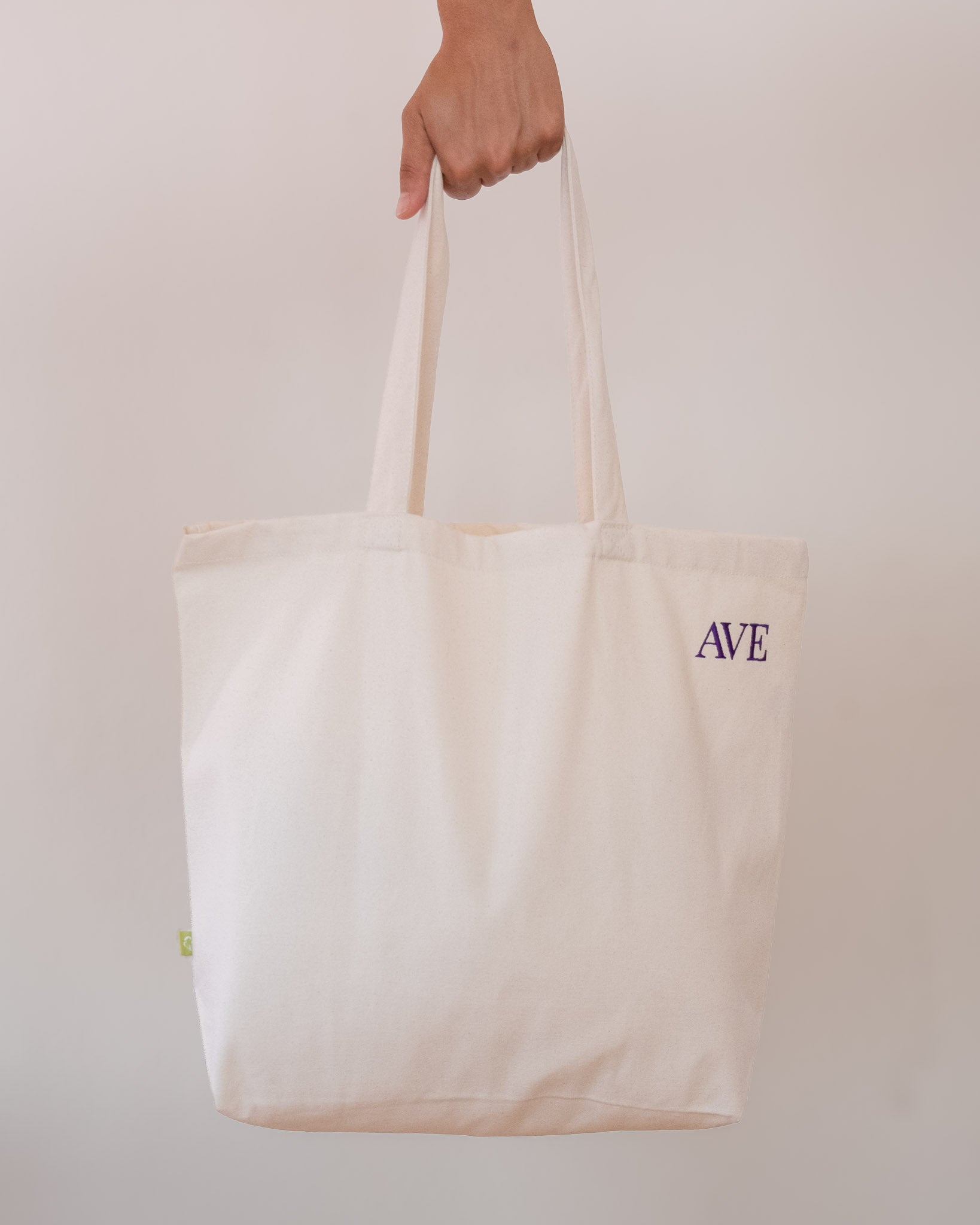 AVE tote bag in beige, held by hand, AVE embroidery in the corner