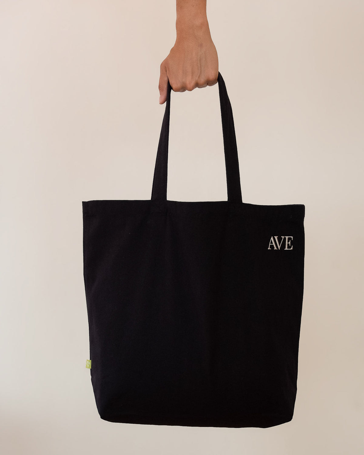 AVE tote bag in black, held by hand, AVE embroidery in the corner