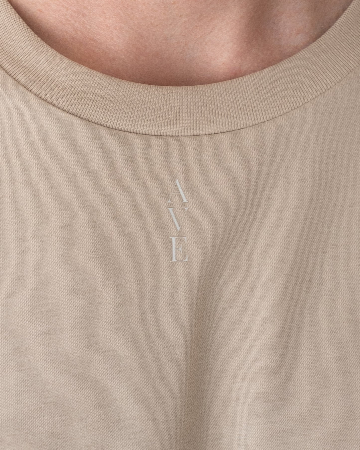 Close up of the neckline of the TESSERA t-shirt in sand , AVE lettering close