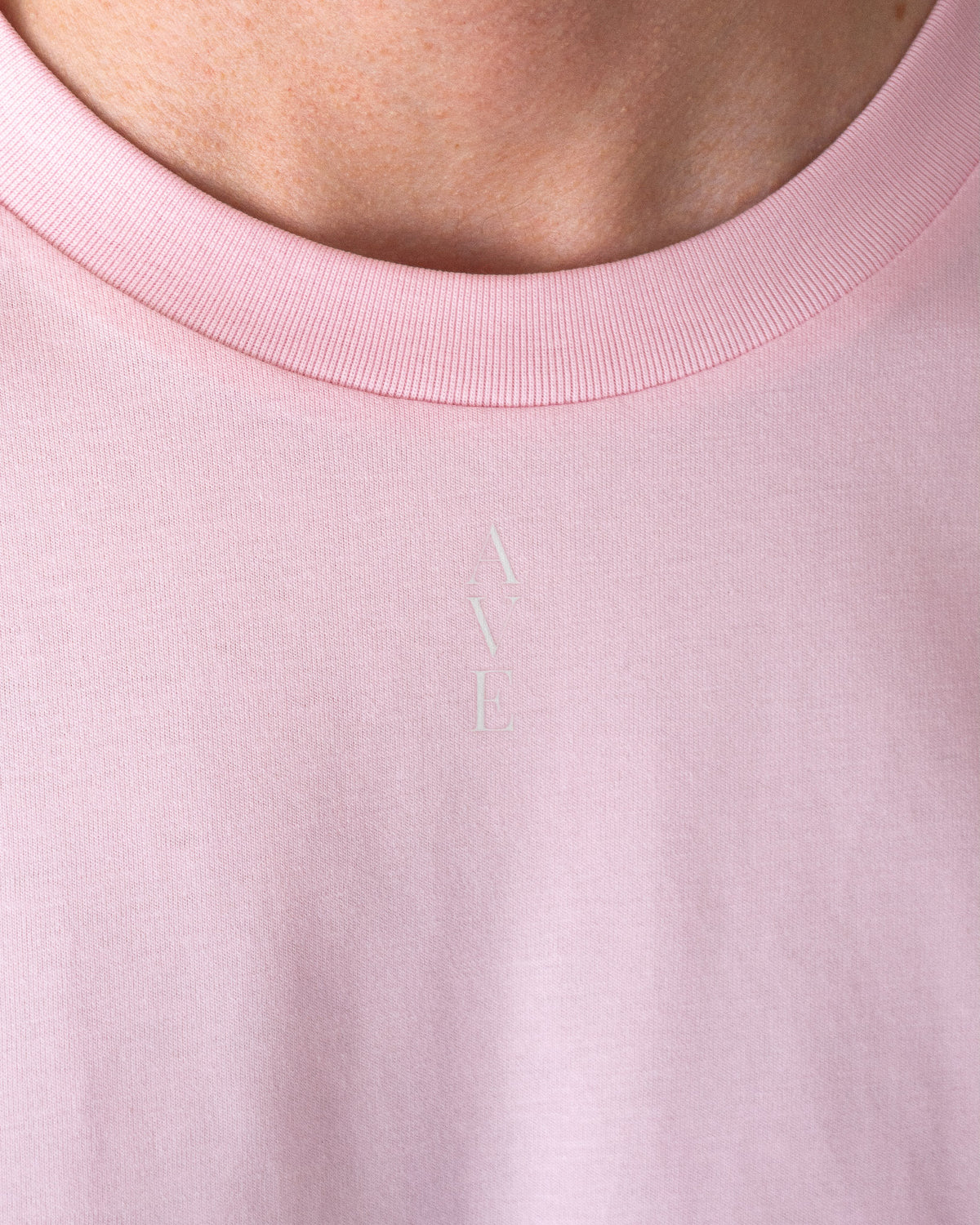 Close up of the neckline of the TESSERA t-shirt in pink, AVE lettering close